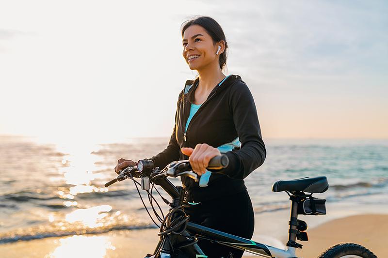 riding a bike near a sunny beach while smiling and wearing earbuds